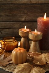 Many different burning candles and dry leaves on wooden table, closeup. Autumn atmosphere