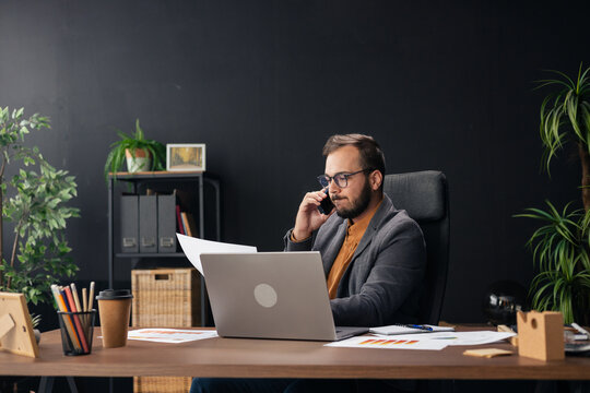 Businessman talking on phone and working on laptop in office - Powered by Adobe