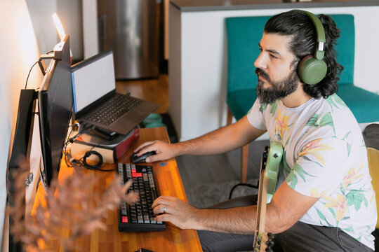 Man composing music at home studio using computer and guitar