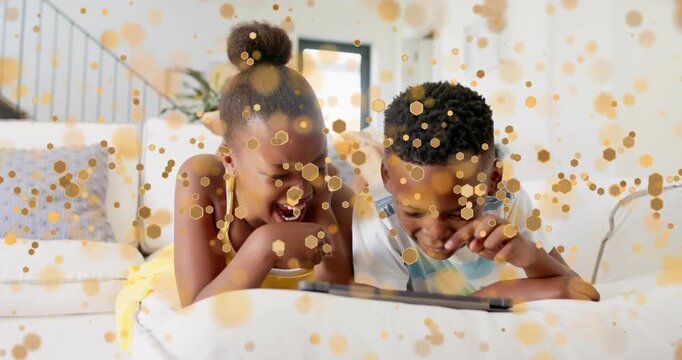 siblings lying on white sofa pointing and tapping tablet with golden sparks drifting for tech demo