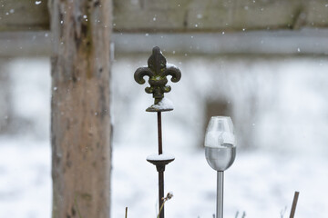 ein Ornament aus Gusseisen neben einer elektrischen solar Fackel Detailaufnahme close-up im Winter im Schnee vor einem Zaun aus L&auml;rchenholz