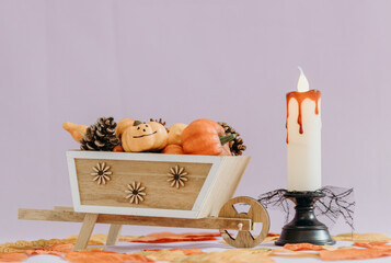Halloween candle with a cart of pumpkins and pine cones on a light background.