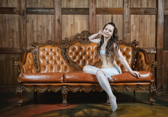 Beautiful sensual woman wears vintage underwear sitting on the brown leather sofa