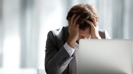 Businessman feeling overwhelmed by a mistake, sitting at a desk with laptop, hands on head. Concept of office stress and problem management