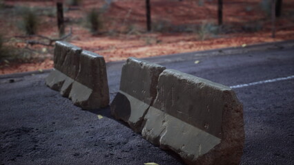 Over an empty road in a desolate landscape, two large stone barricades stand prominently. The red earth and sparse vegetation highlight the harsh environment and isolation.