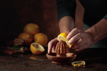 Chef squeezes juice from fresh lemons using an old wooden juicer.