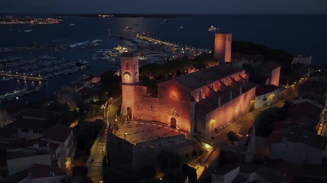 Aerial drone view of Cannes Old Port and the medieval Suquet quarter, with yachts docked in the marina and the Church of Our Lady of Esperance beautifully illuminated