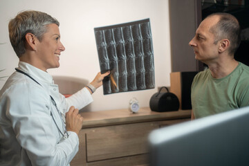 Confident female doctor consulting with mature male patient while looking at x-ray or MRI, concept...