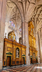 Obraz premium The Segovia Cathedral interior showcases towering Gothic arches and an ornate vaulted ceiling. Massive columns frame the central altarpiece and detailed stained glass