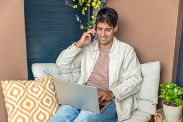 Young Hispanic man teleworking on laptop and talking on phone
