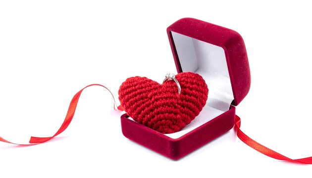 A red heart-shaped crochet with a ring inside a velvet jewelry box, ribbon extends out. Isolated against a white background
