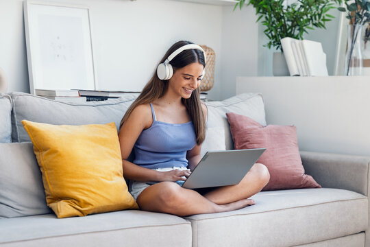 Beautiful gitl working with her laptop while listening to music with earphones sitting on a couch at home