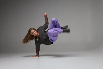 Female teen caucasian dancer in purple pants performing breakdance move in studio