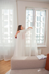 Woman Hanging Sheer White Curtain at Home Interior Design and Window Decoration Concept