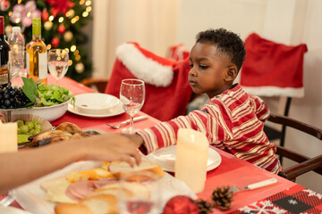 Young Black boy reaching for appetizers on a festively decorated Christmas dinner table. Holiday...