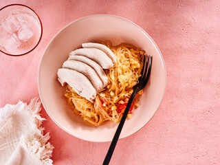 Colorful bowl features tender rice noodles layered with juicy turkey slices, creating a healthy meal perfect for lunch or dinner on a pink table setting