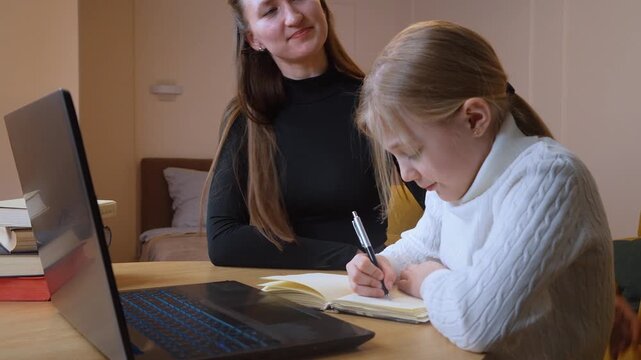 Elementary school student diligently writing in notebook while teacher providing personalized guidance, utilizing laptop and reference books for comprehensive learning support