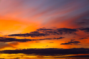 A stunning close-up of the sunset sky showcases an intense blend of brilliant orange, yellow, and deep red. Streaks of dark clouds create a striking contrast against the glowing light, adding drama to
