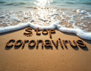 The words Stop Coronavirus are written in sand. The message on the beach faces the sea with waves. Concept of the global pandemic travel restiction.
