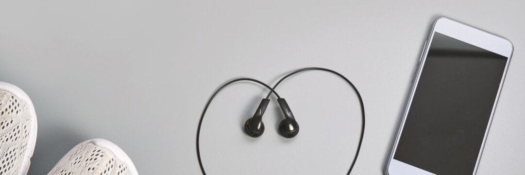 Earphones shaped heart next to smartphone and sneakers on gray background. - Powered by Adobe