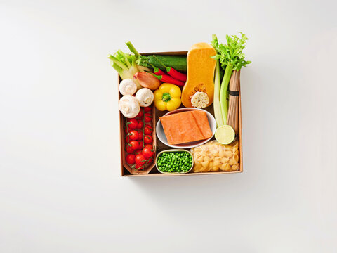 A selection of fresh vegetables and salmon fillet is neatly arranged in a box, showcasing vibrant colors and healthy options ready for cooking