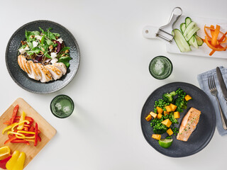 Two beautifully arranged plates of food feature grilled salmon and chicken alongside colorful vegetables. Fresh greens and sliced cucumbers are included for a healthy meal experience