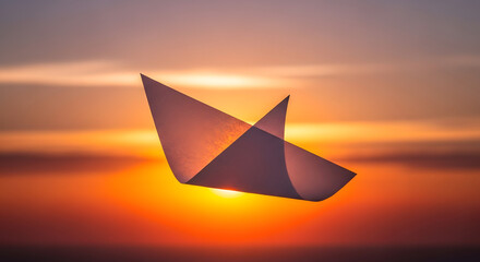 Paper boat sails on sunset horizon with warm light.