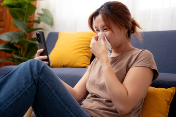 Obraz premium Women have the flu and a runny nose, and feel sick and cold. Sick Asian woman sitting on the floor. Concept of cold, flu, allergy,