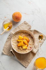 Oatmeal with peaches and nuts  in a bowl on a marble background with honey