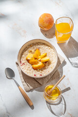 Oatmeal with peaches and nuts  in a bowl on a marble background with honey