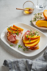 Toast with peach, cream cheese, ham and honey on a plate on a light background