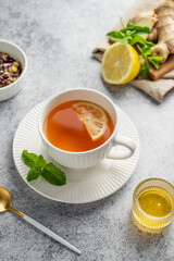 Tea with lemon, ginger, honey, and mint in a cup on a gray background with citrus fruits and herbs.