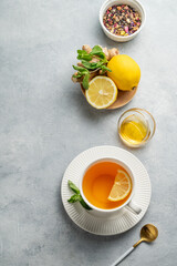 Flat lay of hot tea with lemon, ginger, honey, and mint in a cup on a light background