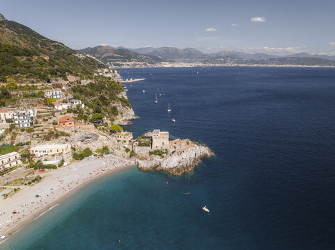 Aerial view of the Torre La Cerniola standing guard over the sun-kissed beach, where turquoise waters meet the golden sand, shadowed by mountainside villas, Erchie, Amalfi Coast, Campania, Italy.