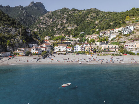 Aerial view of the tranquil beach where the Tyrrhenian Sea meets the rugged cliffs of Erchie, with buildings nestled amongst the green hillsides, Erchie, Amalfi Coast, Campania, Italy.