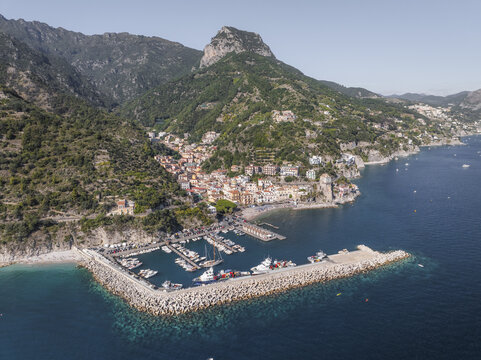 Aerial view of boats nestled in the harbor, a protective arm of concrete embracing the azure sea against the backdrop of rugged cliffs, Cetara, Amalfi Coast, Campania, Italy.