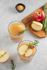 Two glasses of hot apple cider with cinnamon, anise, and rosemary on a light background