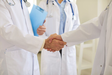 Cropped shot of two doctors in white lab coats shaking hands in clinic. Medical staff exchanging...