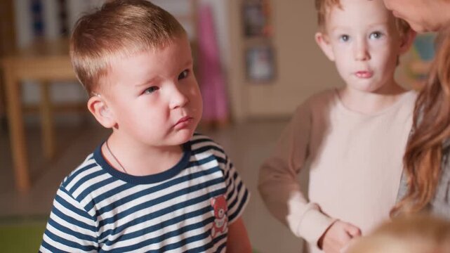Close up of adult holding tortoise during classroom session as child in striped shirt with hearing aid listens attentively while another child in beige shirt answer question about animal behavior