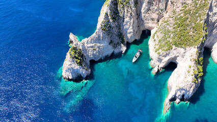 Aerial drone top down photo of inflatable rib boat anchored in paradise volcanic white cliff cove with crystal clear emerald sea and scenic caves © aerial-drone