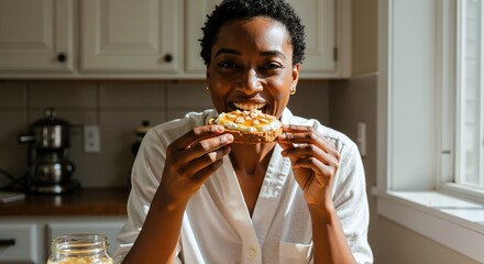 Happy Black woman eating toast for breakfast in sunlit kitchen. Young female enjoying healthy morning snack at home. Simple pleasures and wellness lifestyle