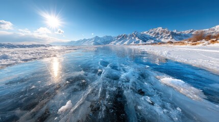 Obraz premium A breathtaking view of a frozen lake with crystal-clear ice, surrounded by majestic snow-capped mountains, illuminated by a clear blue sky and radiant sunlight.