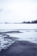 Frozen lake landscape with melting ice and bare trees in winter season