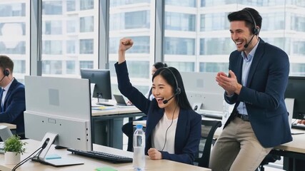 Excited call center agent with headset celebrating a sales success with a fist pump as her happy colleague applauds her in the modern office. - Powered by Adobe