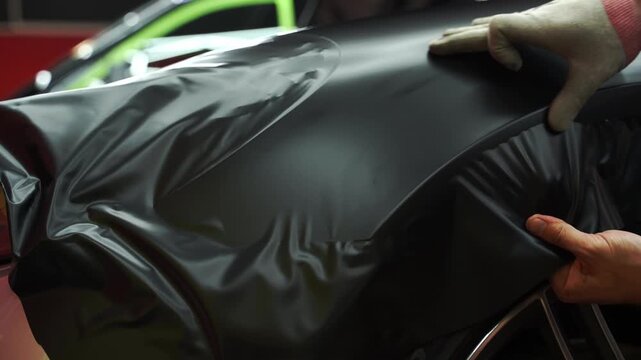 Matte black vinyl wrapping around car with smooth alignment over curves and edges 4k video. Matte black vinyl wrap application on front fender and wheel arch of luxury vehicle. Vinyl Wrapping of Car.