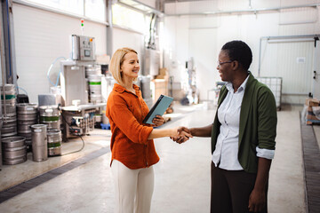 Fototapeta premium Businesswomen shaking hands in brewery warehouse