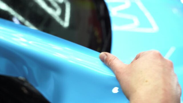 Applying PPF wrap on car during full detailing 4k video. Bold blue vinyl wrap installing in detailing center. Detailers expertly apply wrap to fit contours and ensures smooth, flawless wrap alignment.