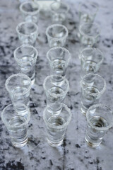 Neatly arranged shot glasses with a salt rim, filled with clear alcohol, prepared for a party or celebration on a stylish grey background