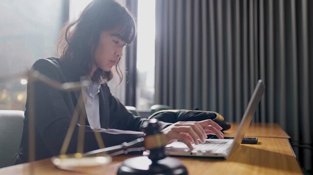 Young legal advisor woman typing on laptop at modern office desk with gavel, law and consulting concept.