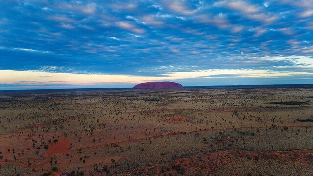 Majestic Uluru, the iconic red sandstone monolith, rises against a dramatic sky at sunset in the Australian outback.